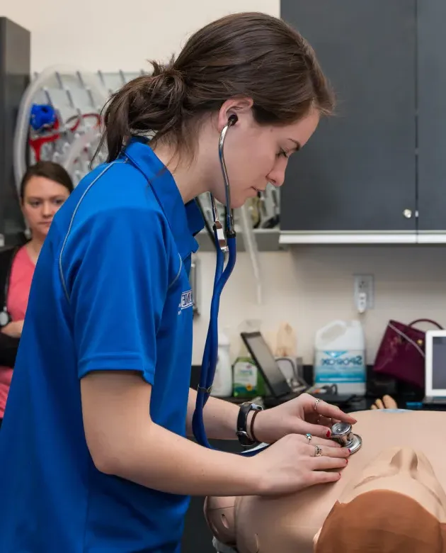 A student uses a stethoscope on a patient simulator